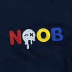 NOOB Multi Logo embroidered on the font of a navy t-shirt showing close up of stitching.