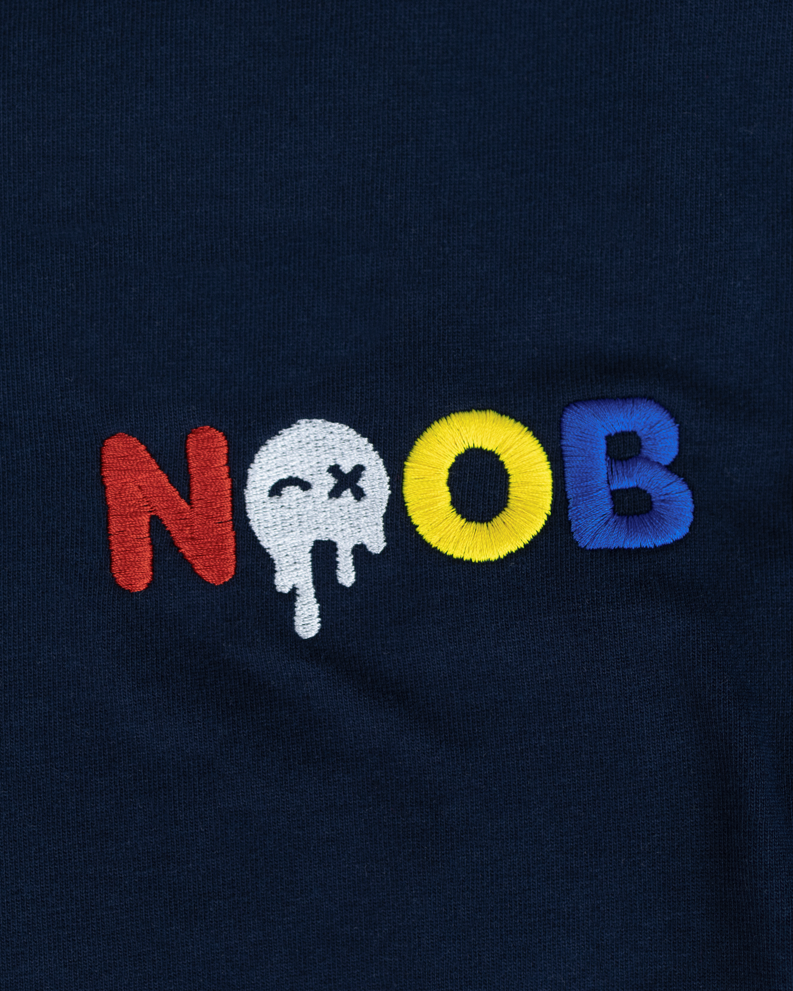 NOOB Multi Logo embroidered on the font of a navy t-shirt showing close up of stitching.