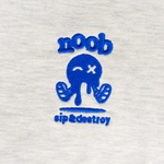 NOOB Spanky Logo embroidered in blue on the font of a heather oatmeal t-shirt showing close up of stitching.