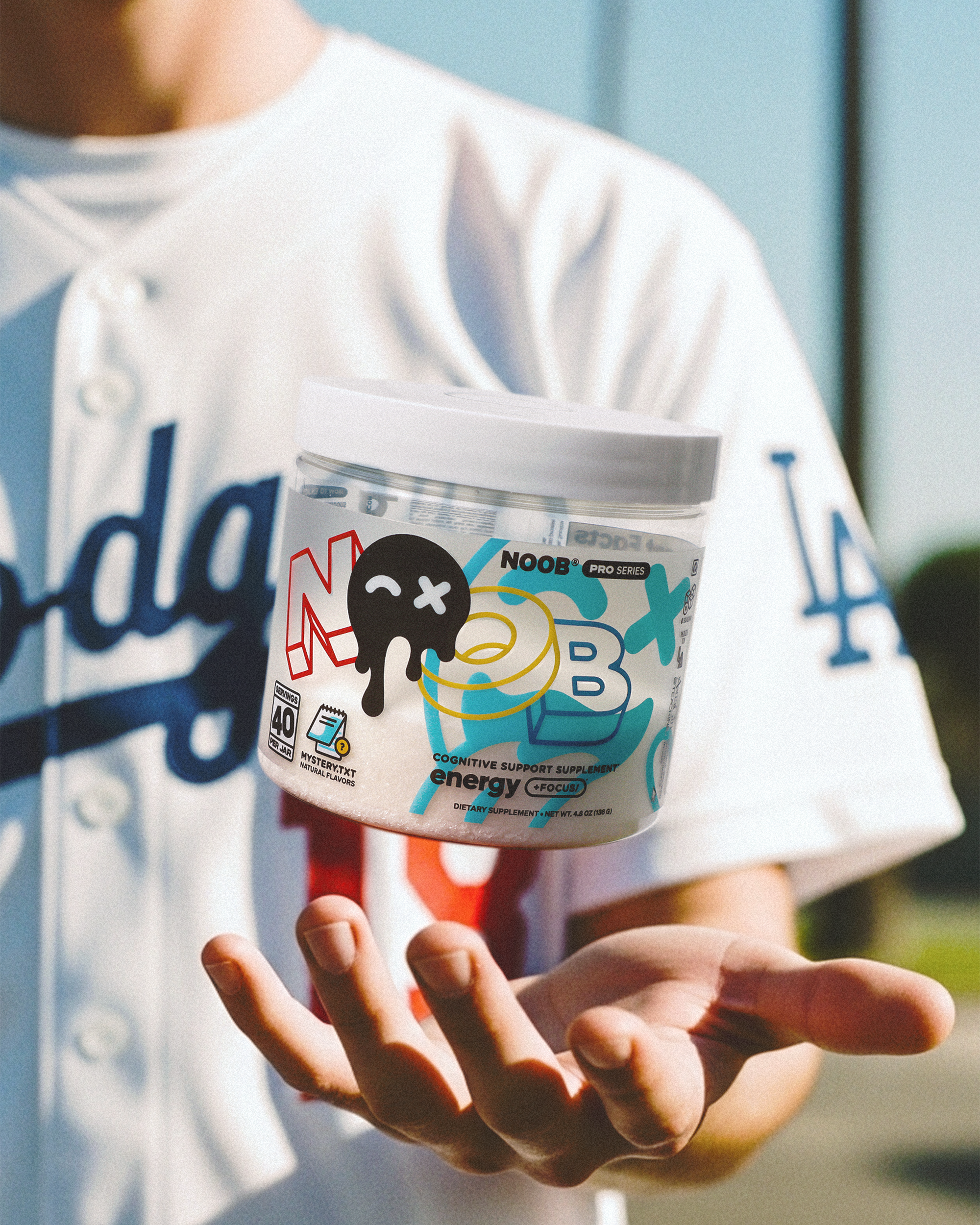 Person holding a container of NOOB energy supplement in front of a blurred background